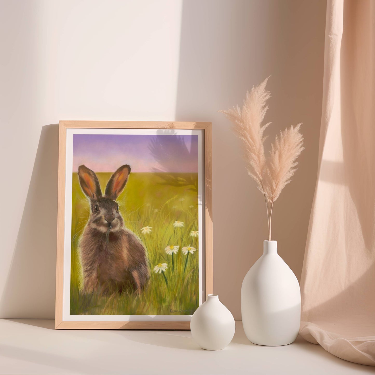 Framed artwork of a hare in a field with two white vases on a shelf.