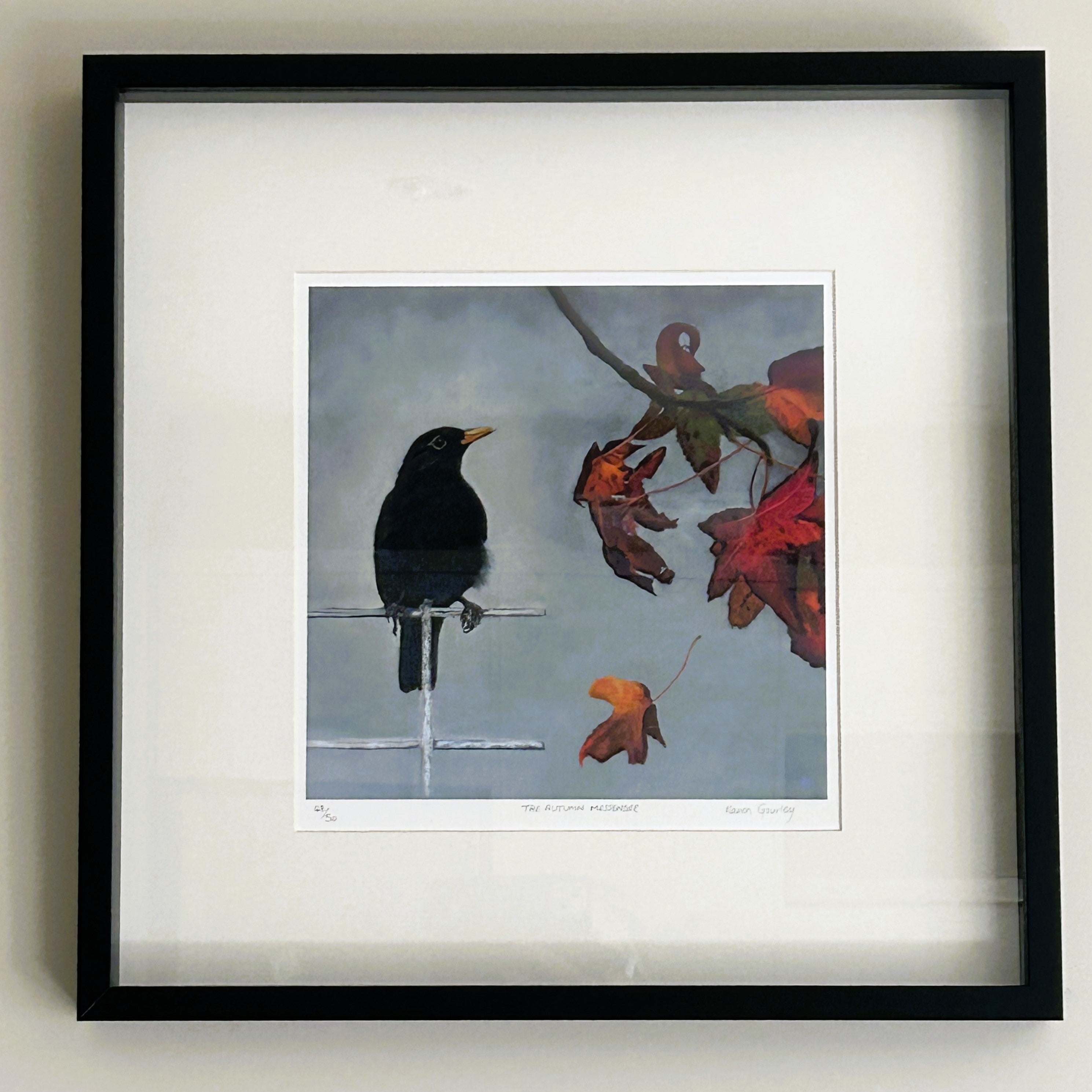 Framed artwork of a black bird on a branch with red flowers on a light gray wall.