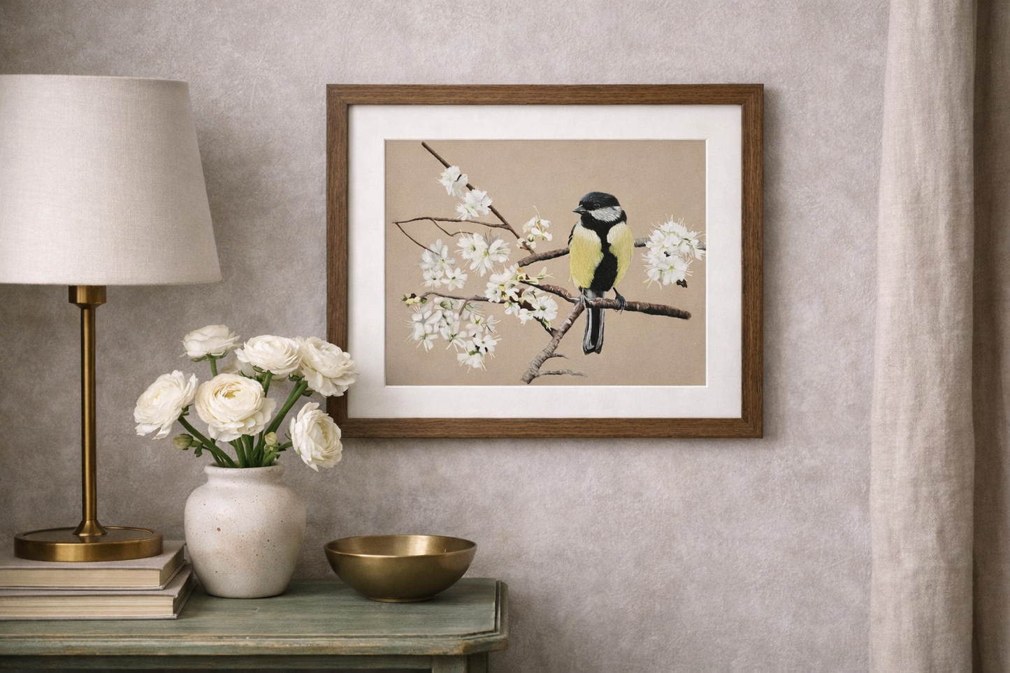 Framed artwork of a bird on a branch with flowers, placed on a wall above a table with decor items.