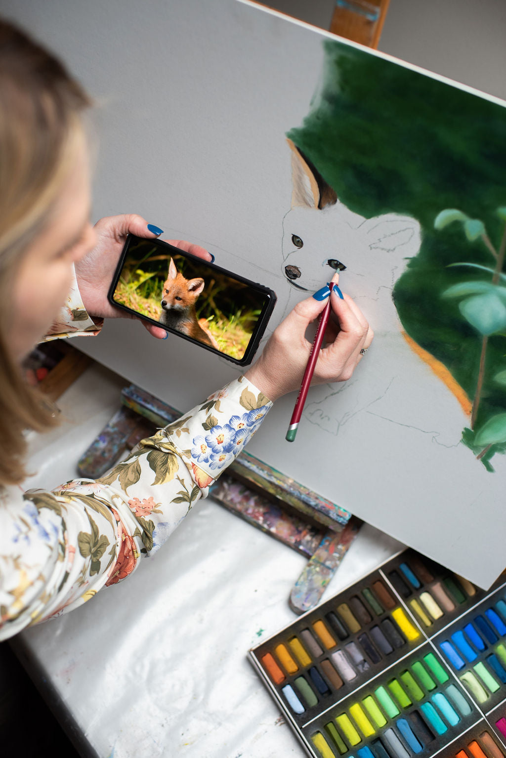 Karen Gourley at her easel painting a fox cub in pastel using a photo reference on her phone — the commission process in action