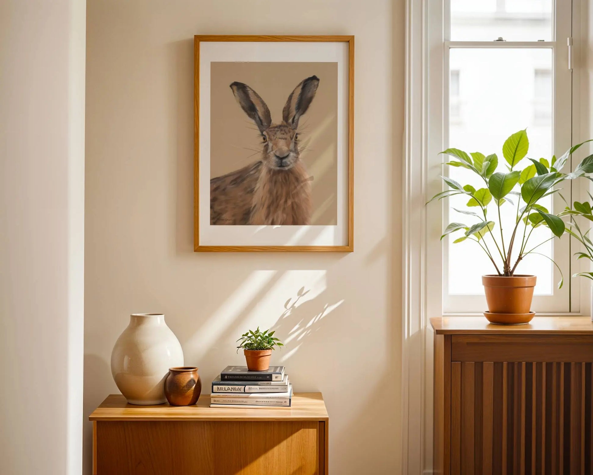 Framed picture of a hare on a wall above a wooden side table with books and a vase.