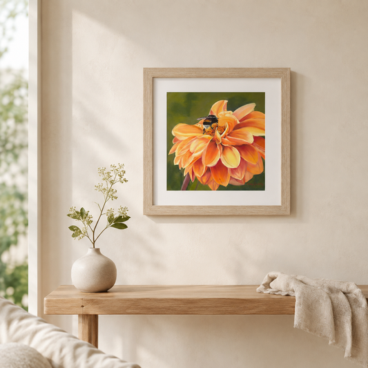 A framed art print of an orange dahlia flower with a bumblebee, displayed on a beige wall above a wooden console table with a vase and a throw blanket.