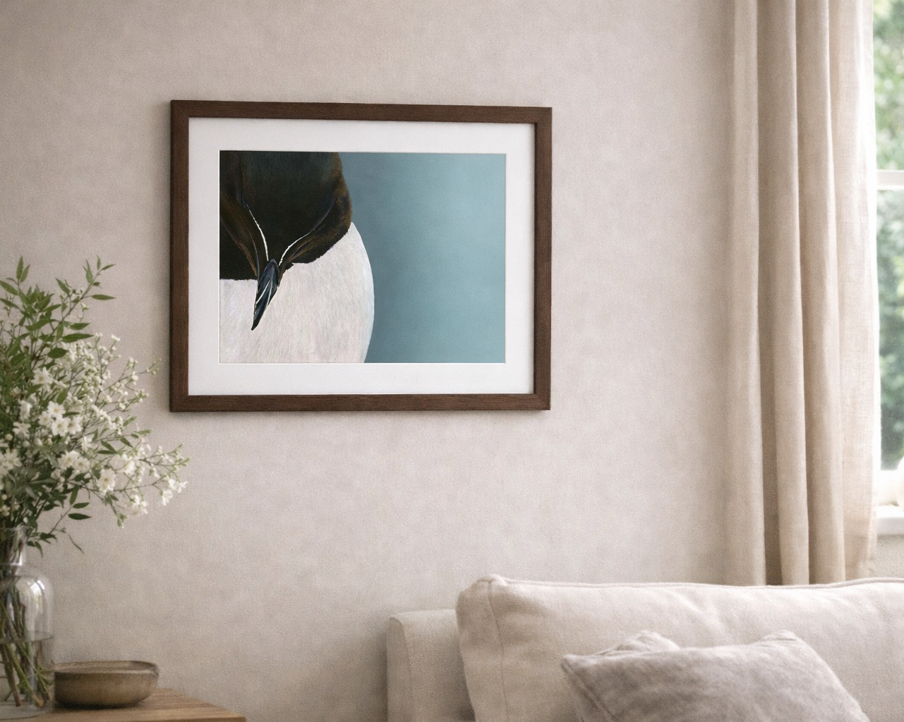 Framed artwork of a bird on a wall in a living room with a couch and decorative items.