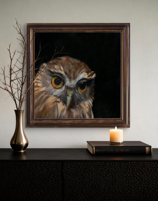 Framed painting of an owl on a wall above a dark surface with a candle and vase.