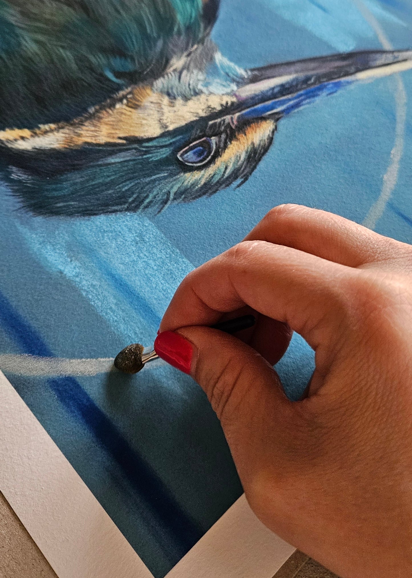 Hand with red nail polish painting a detailed bird illustration on paper.