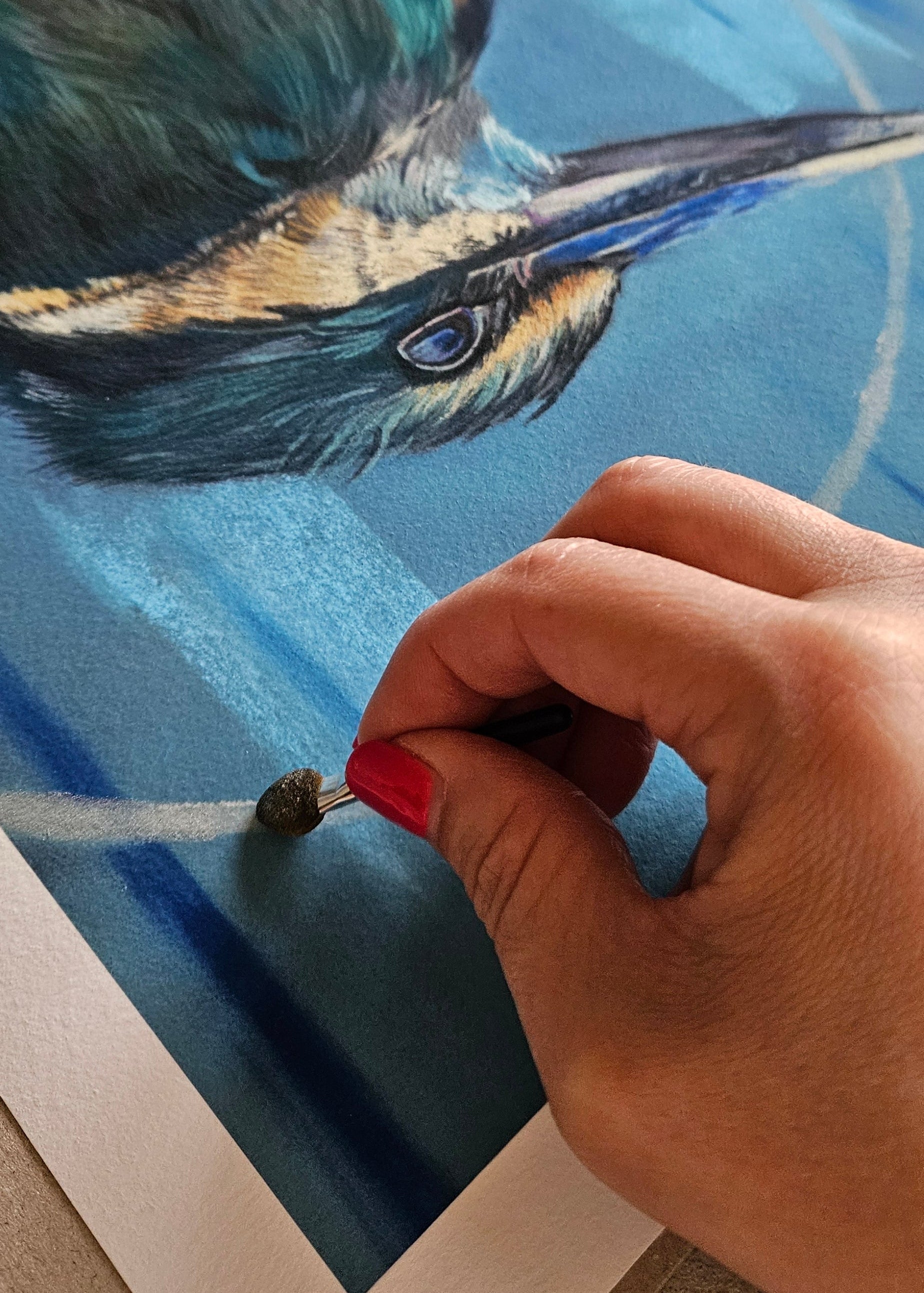 Hand with red nail polish painting a detailed bird illustration on paper.