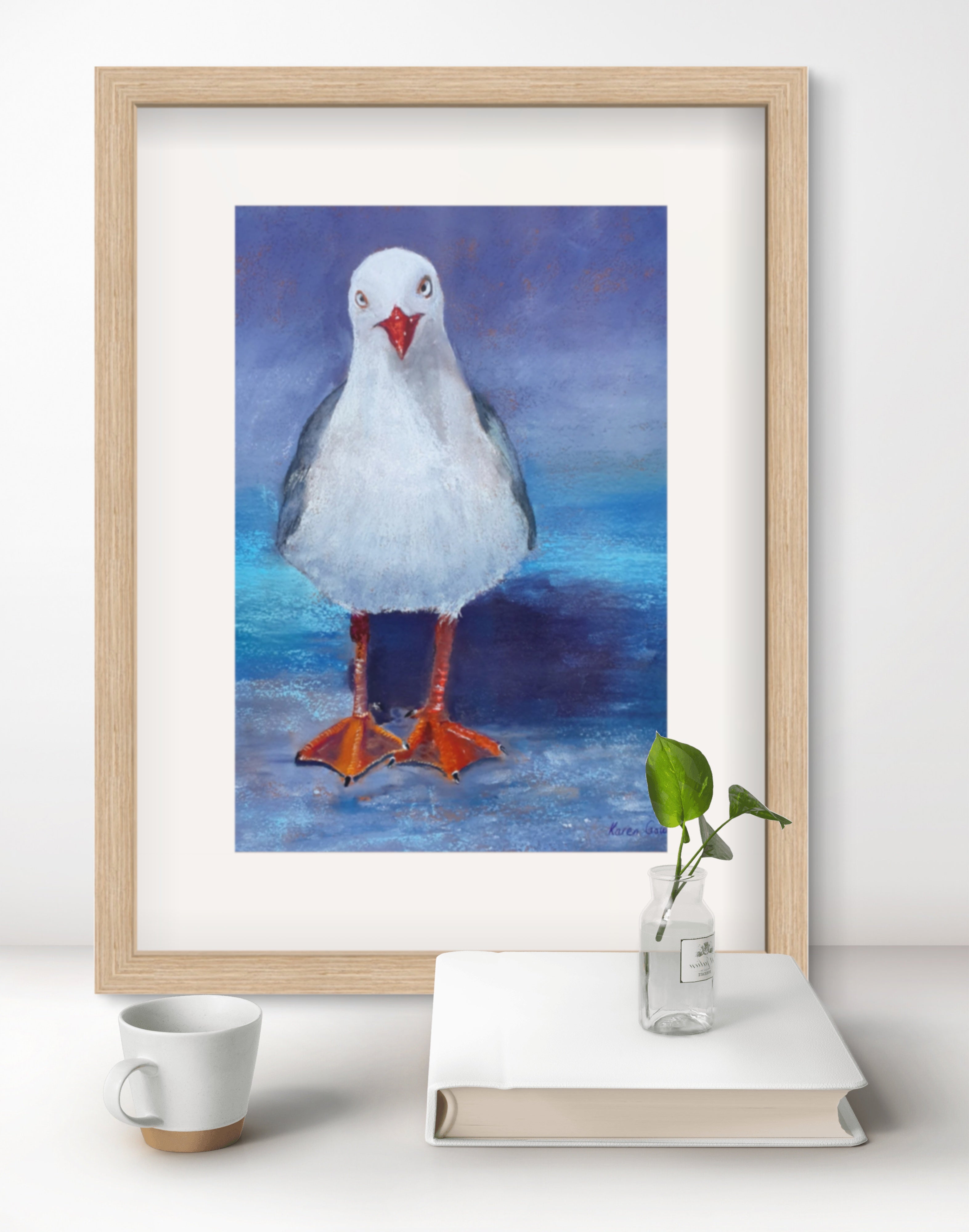 Framed artwork of a seagull on a shelf with a cup and plant.